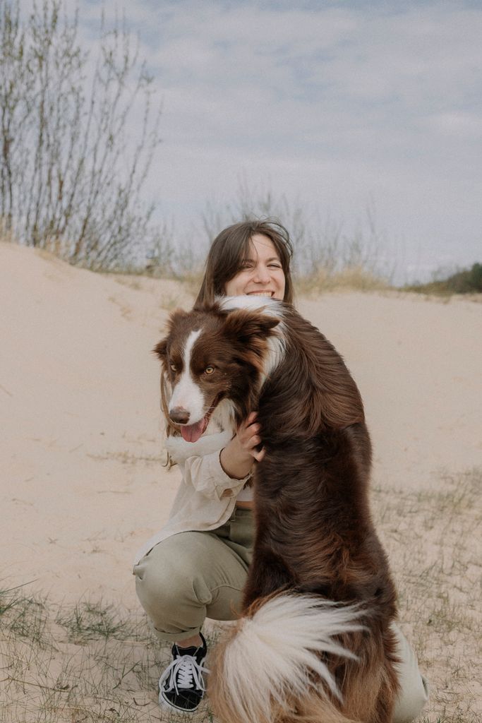 A woman joyfully hugs her Border Collie in a serene sandy setting, showcasing companionship.