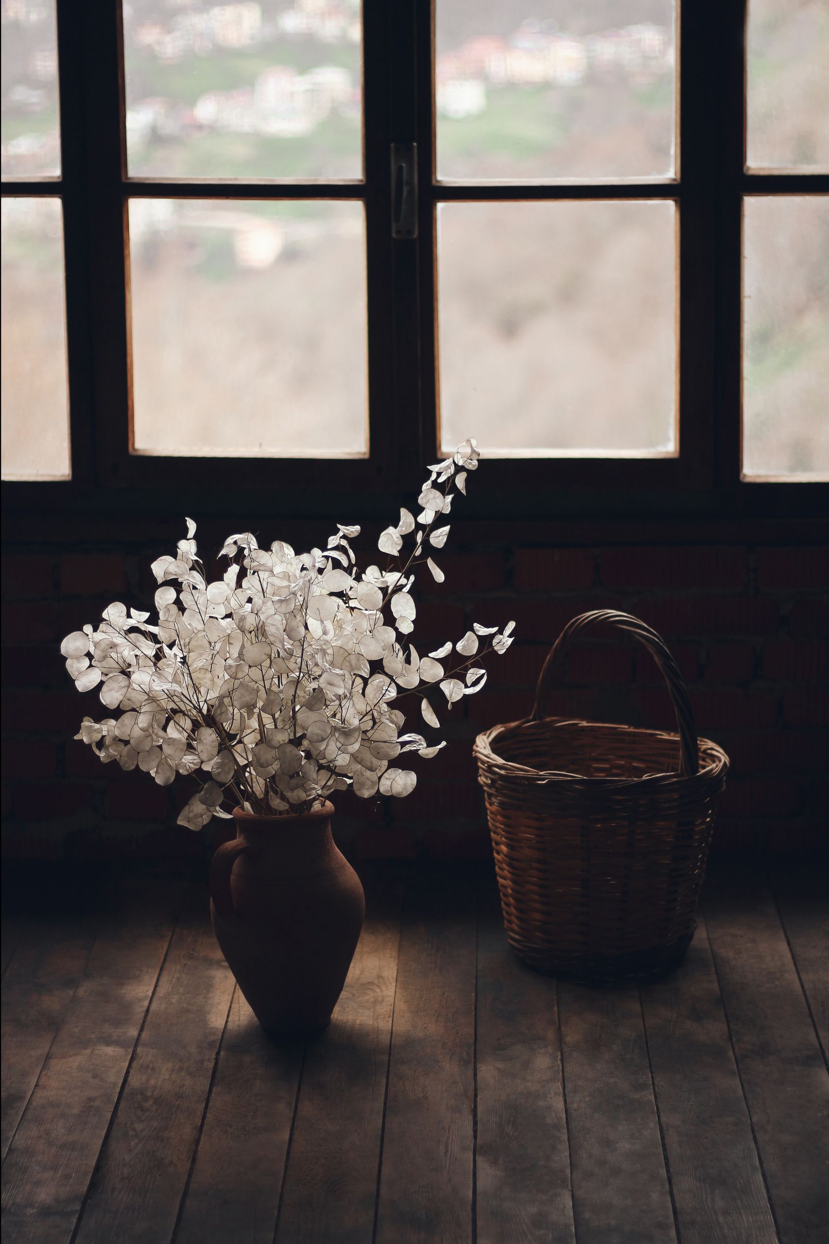 A cozy rustic interior featuring a vase with flowers and a wicker basket by an old window.
