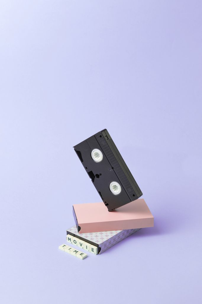 Old VHS tape with scrabble tiles and pink box on light purple background. Retro vibes.